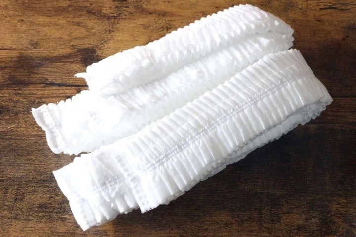 木目の床に未着用の白い不織布まくらカバーが折りたたまれて並べられている俯瞰写真