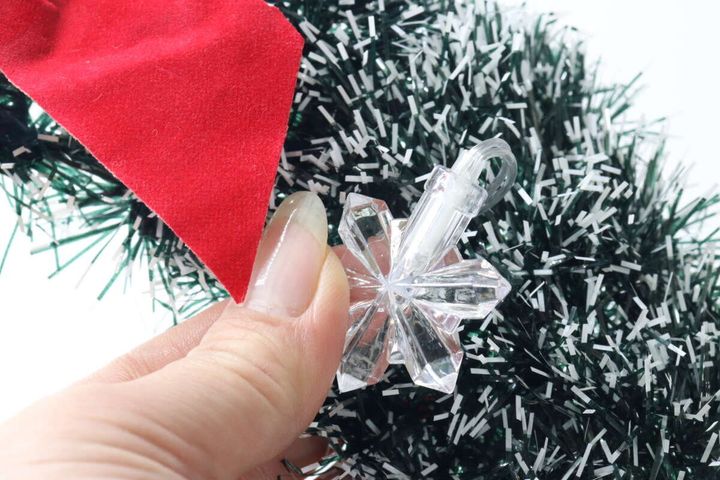 クリスマスリースに雪の結晶型のデコレーションライトを組み合わせるため、指で持っている。