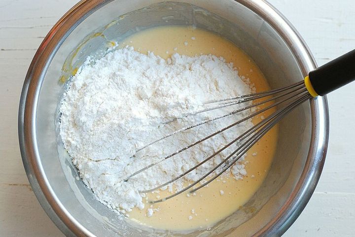ステンレスのボウルに入った生地に泡立て器を合わせホットケーキミックスを加えている工程