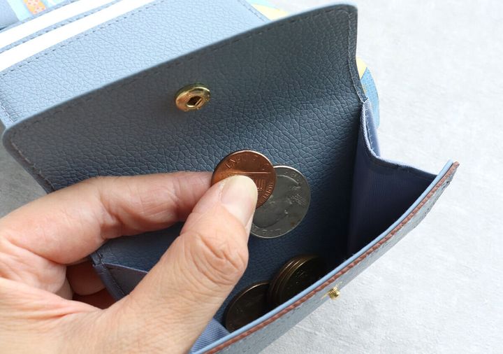 サックスブルーのミニ財布の小銭入れから硬貨を取り出す手元