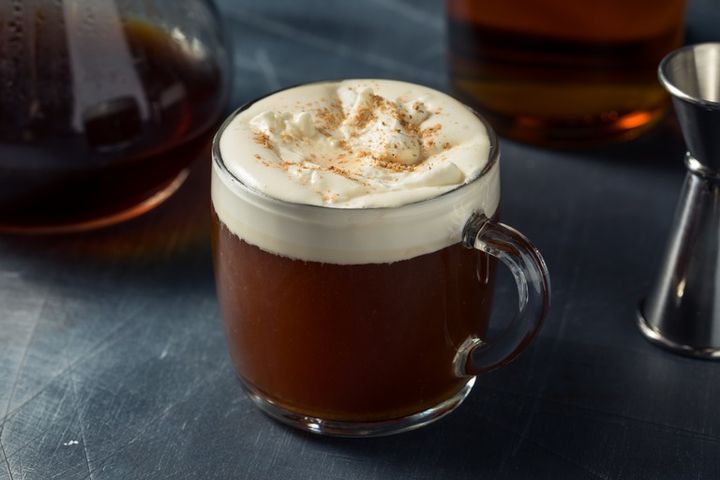 ガラスマグに入ったアイリッシュコーヒー 背景にガラスポットに入ったコーヒーとウイスキーが映る