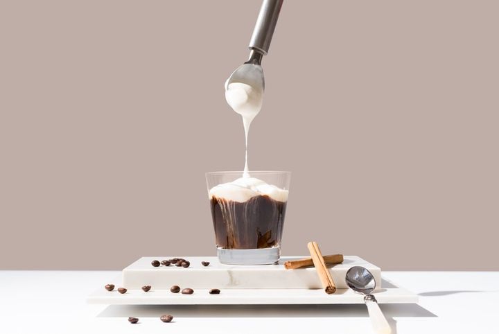 コーヒーに生クリームを乗せる様子 シナモンとコーヒー豆が散らばる