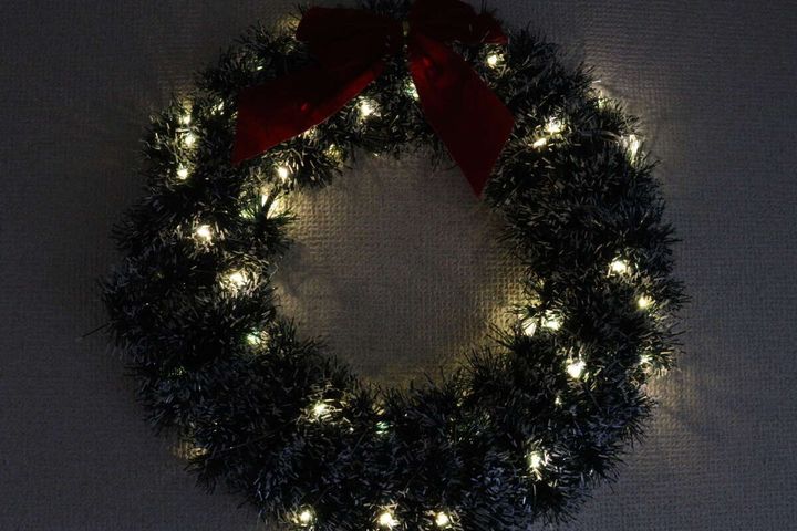 クリスマスリースにストリングライトを巻き付け、暗い部屋で点灯させた様子。