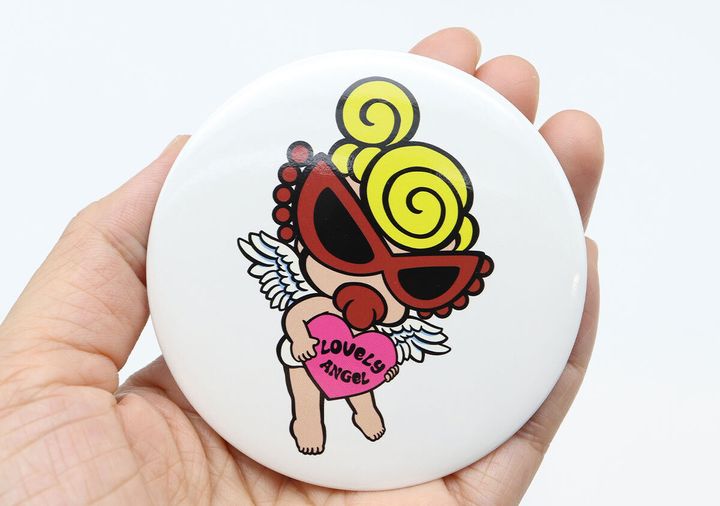 ヒステリックミニのANGEL MINIがデザインされた白い缶バッジを手のひらに乗せている