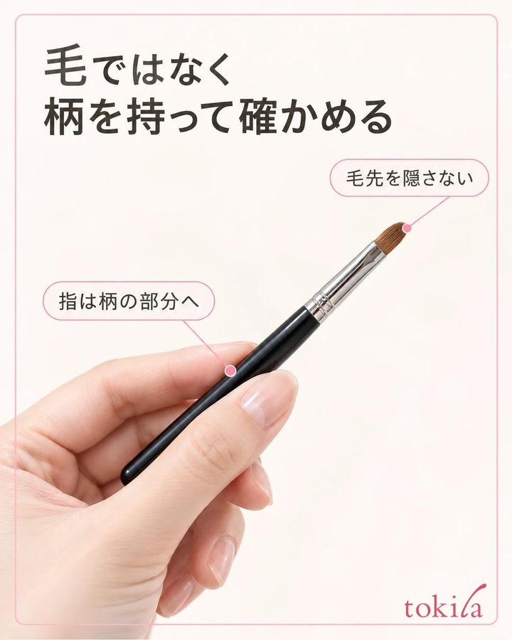 乾いた成人の指が黒いリップブラシの柄を持ち、先端の毛束と金具から離れている接写
