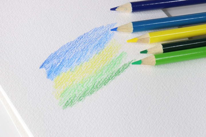 画用紙に青や黄色、緑の水彩色鉛筆で試し描きをしている様子