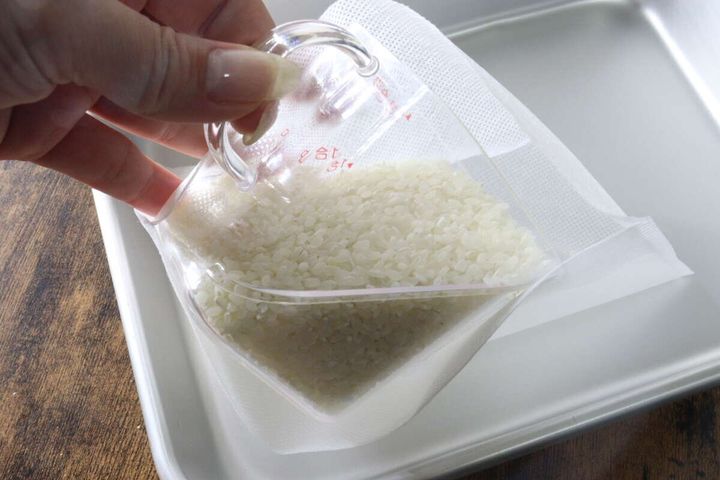 計量カップを使って生米を白い不織布製の炊飯袋に入れている様子