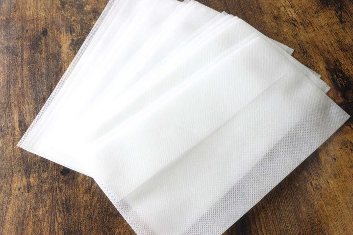 木目の台の上に重ねて置かれた10枚入りの白い不織布製炊飯袋