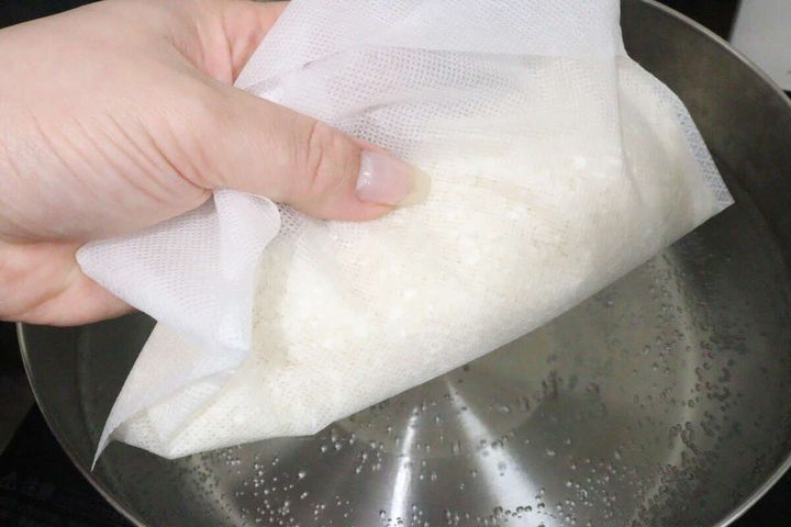 沸騰したお湯を入れた鍋に生米を入れた炊飯袋を投入している手元