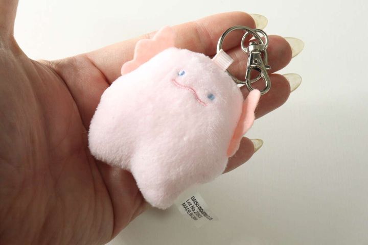 女性の手のひらに乗せられた手のひらサイズのピンク色のマスコット