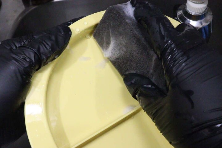 角のあるスポンジ部分を使って黄色の平らなお皿を洗っているところ