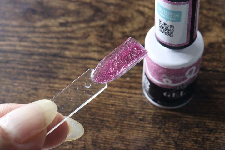 カラーチャートの先端にピンク色のジェルネイルを塗っている様子