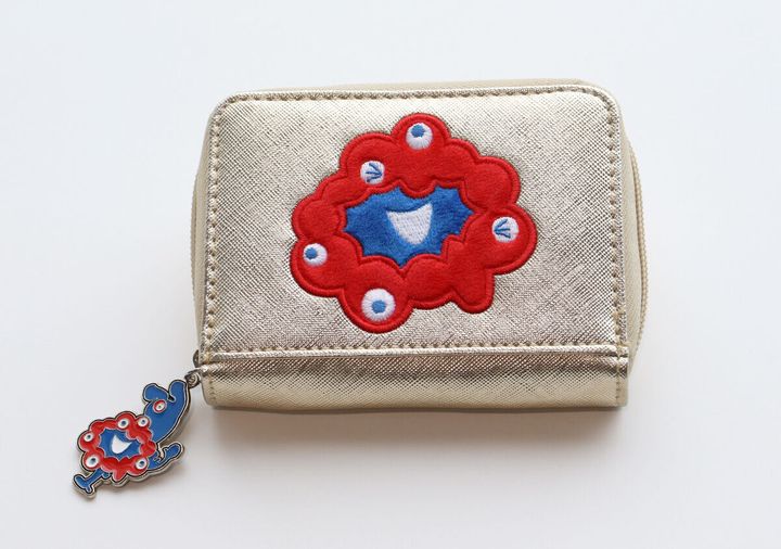 ゴールドのミニ財布の正面アップ。ミャクミャクの赤い刺繍と、ファスナーの引き手についたミャクミャクのチャームが見える