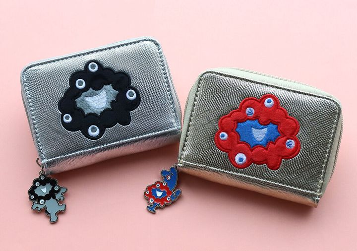 ゴールドとシルバーのミャクミャクミニ財布が、ピンク色の背景の上に並んで置かれている