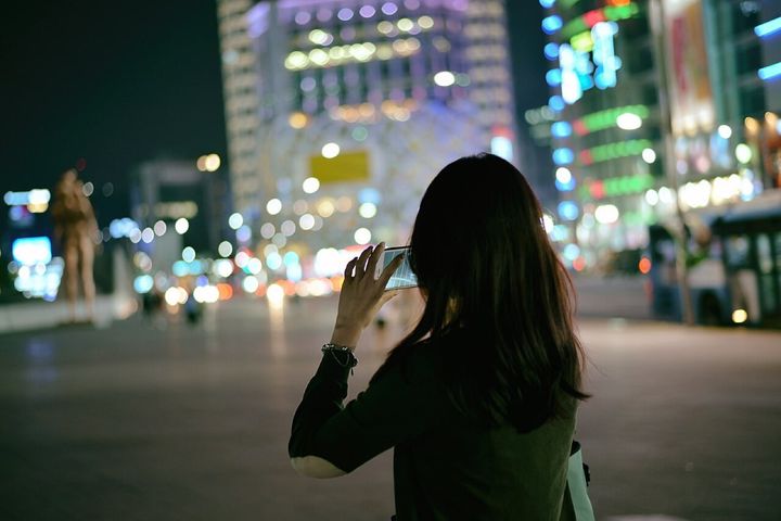 夜の街で、スマートフォンを使って写真を撮る女性です(韓国・ソウル)。のめり込み具合は、最初に用意した10問から、統計的な確認を経て残った6問で測られました。