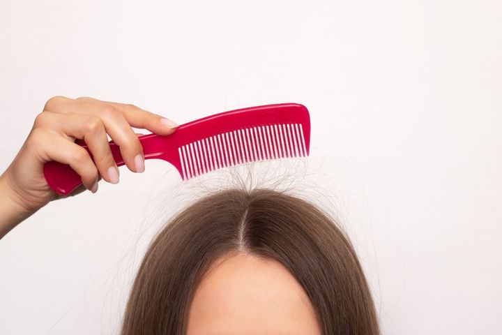 くしを頭の上にかざす女性 髪の毛が静電気でブラシにくっついている様子