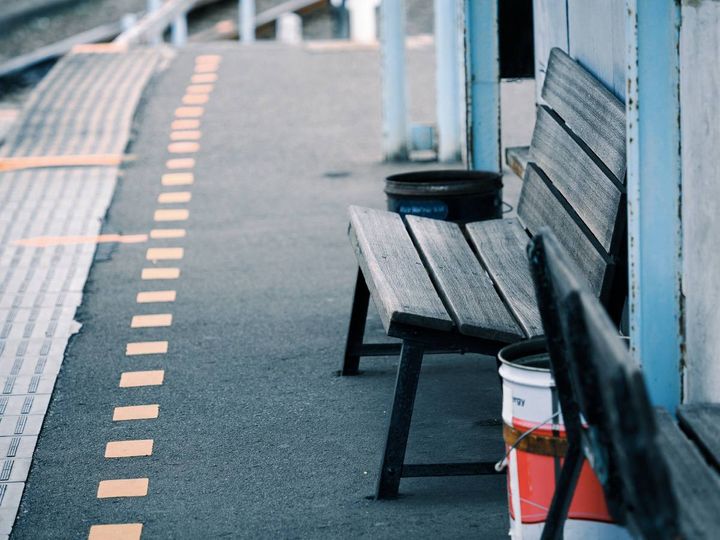 駅のホームに設置された古い木製ベンチ。奥には線路沿いに続くホームが見える。
