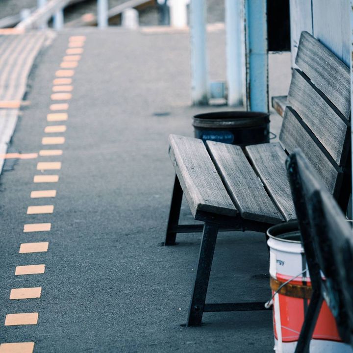 駅のホームに設置された古い木製ベンチ。奥には線路沿いに続くホームが見える。