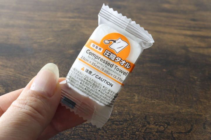 個包装された小さな圧縮タオルを1個手に持って見せている状態