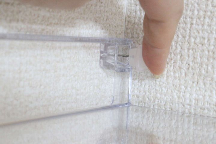 白い壁紙の壁にディスプレイトレーの穴の位置を合わせながら指でピンを押し込んでいる様子