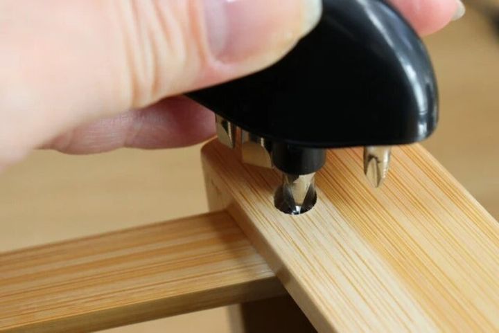 右手がキーホルダー型ドライバーで木製棚のネジを締めている