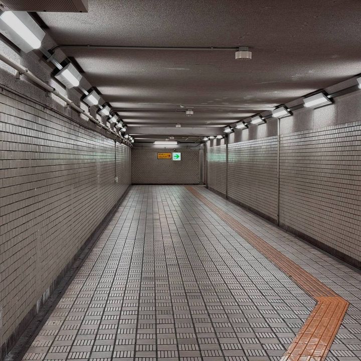 白いタイル張りの壁と床が続く地下通路。天井には照明が並び、床には点字ブロックが敷かれている。