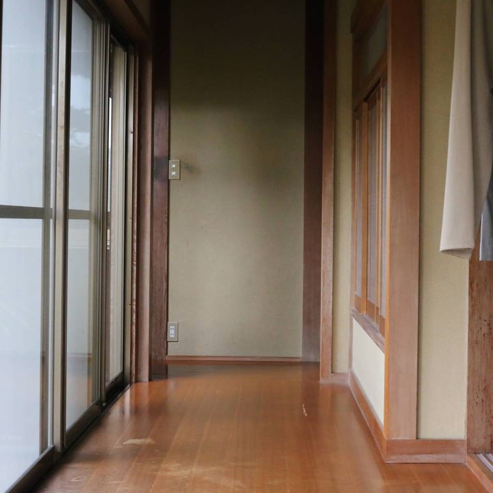 木製の床が続く日本家屋の廊下。左側には庭に面したガラス戸が並び、右側には和室の入り口が見える。