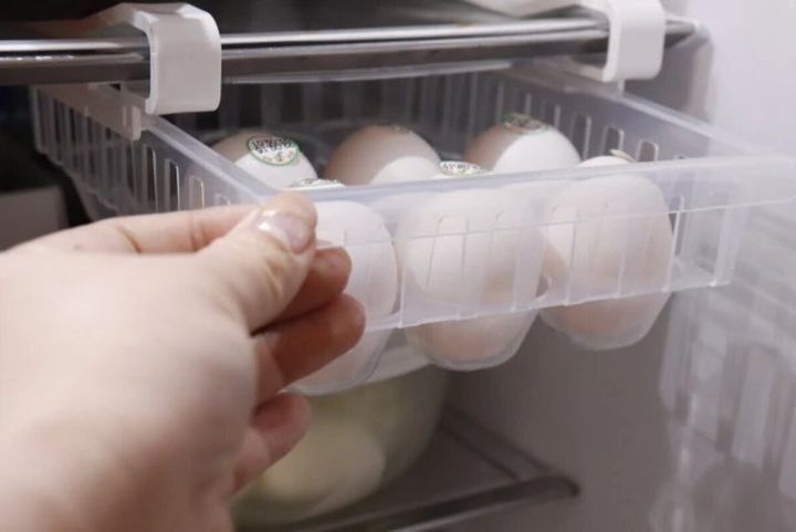 冷蔵庫の棚に設置された吊り下げ収納ケースから卵を取り出している手元