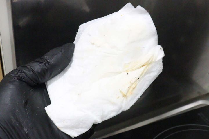 汚れを拭き取ったあとの黄色っぽくなったキッチンペーパーを掲げる手元