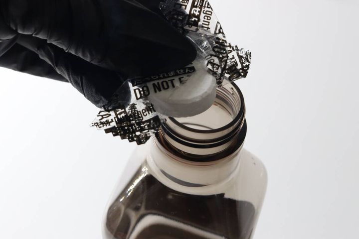 黒い手袋をした手でスプレー容器の口に錠剤を入れている様子