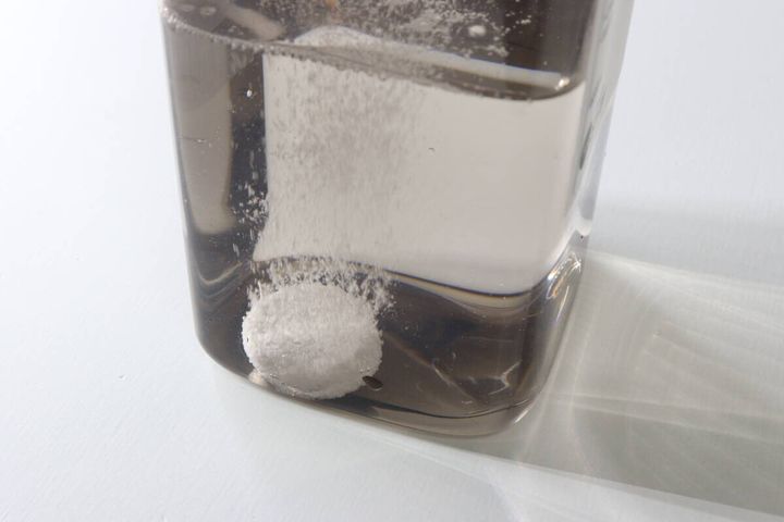 茶色い容器の水の中で錠剤が発泡しながら溶けていく瞬間