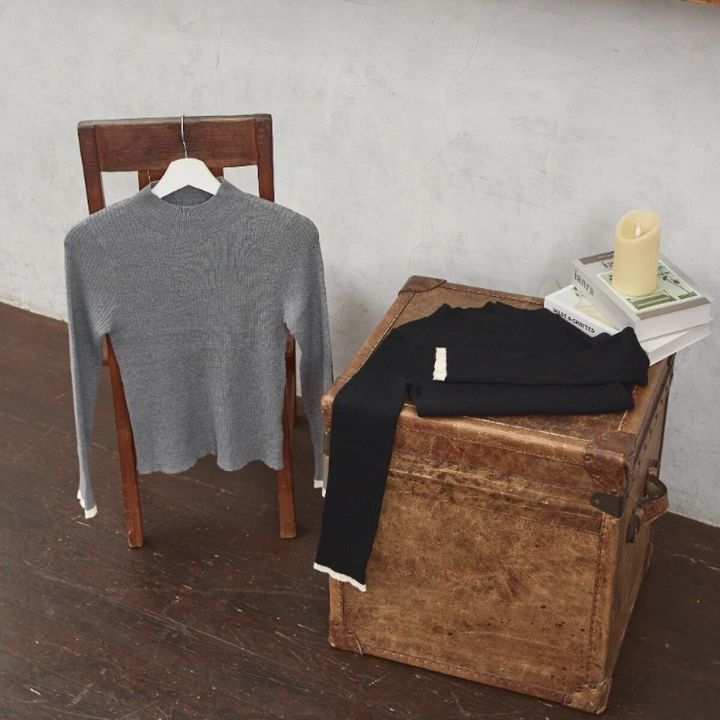 木製の椅子とトランクに置かれたグレーと黒の配色ニットプルオーバー