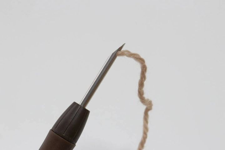 パンチニードルの先端の針穴からベージュ色の毛糸が出ている状態