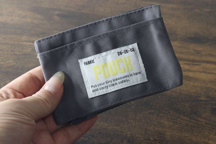 手に持ったグレーのミニポーチの表面にあるおしゃれなタグデザインの様子