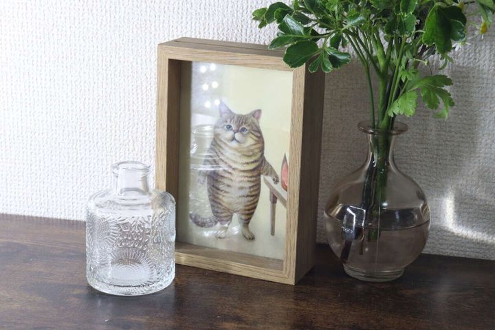 猫の写真立ての横に2種類の花瓶と緑の植物が飾られている棚の上