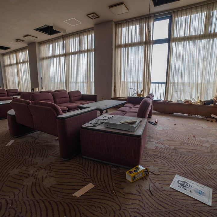 大きな窓にカーテンがかかった、廃旅館のラウンジ。紫色のソファが並び、床には紙くずなどが散乱している。