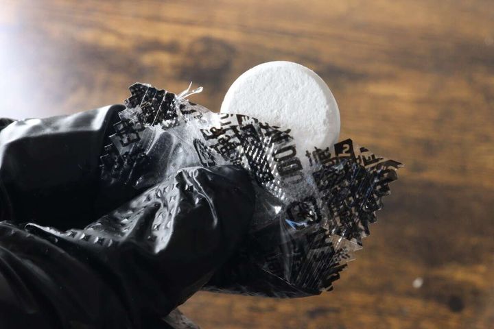 黒い手袋をした手で個包装から白い錠剤を取り出している状態
