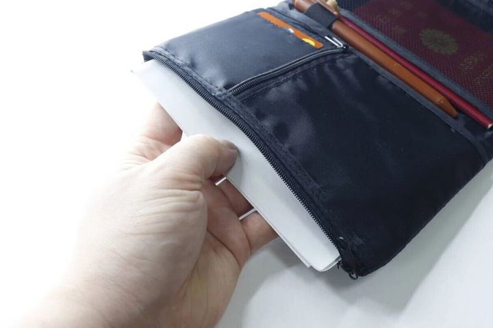 パスポートケースのファスナーポケットに白い用紙を入れている手元