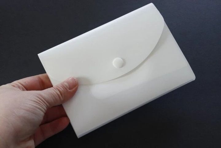 白いスナップボタン付き通帳ケースを手で持っている様子