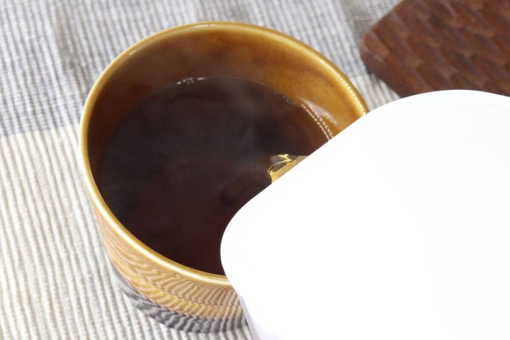 ウォーターポットから茶色いお茶をマグカップに注いでいる瞬間
