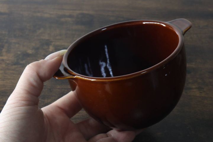 女性がブラウンのスープボウルを片手で持っている様子